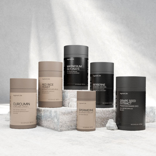 Six cylindrical supplement containers in shades of brown and black are arranged on a stone surface. Labels display ingredients like Cur cumin and Magnesium. The tone is minimal and modern.