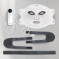 An LED skincare mask set with a white face mask featuring eye and mouth cutouts, a control device, USB cables, and adjustable black straps on a Gray surface.